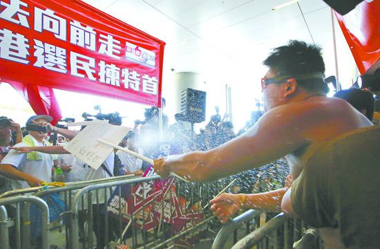 17日，在香港立法會外，一名反對政改的男子向支持派人群投擲標牌。