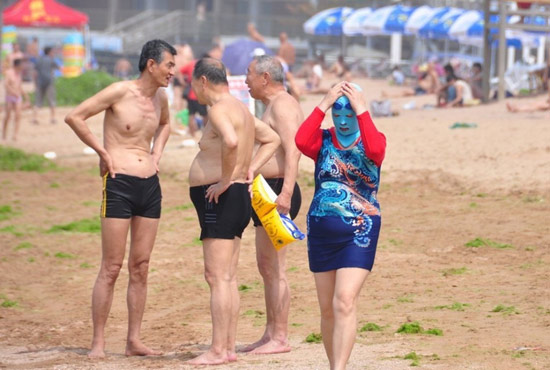 2013年7月3日，山東青島青島高溫來襲，“青島大媽”不懼滸苔，戴著“強盜面具”出現在海水浴場消暑降