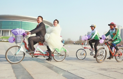 氣球和鮮花裝點(diǎn)的雙人自行車，新郎郝幸福載著美麗新娘回家。